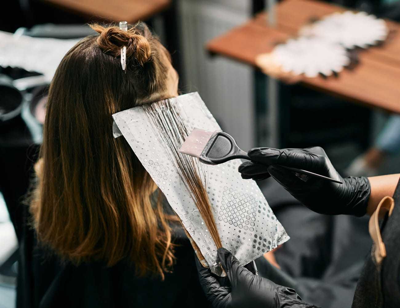 Hairdresser applying color to client's hair with a brush in a salon.