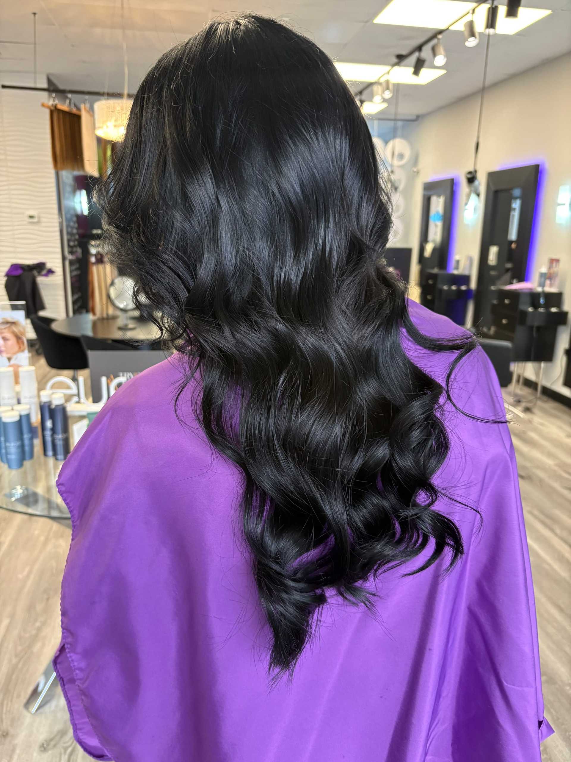 Long, wavy dark hair styled elegantly in a salon chair with purple cape.