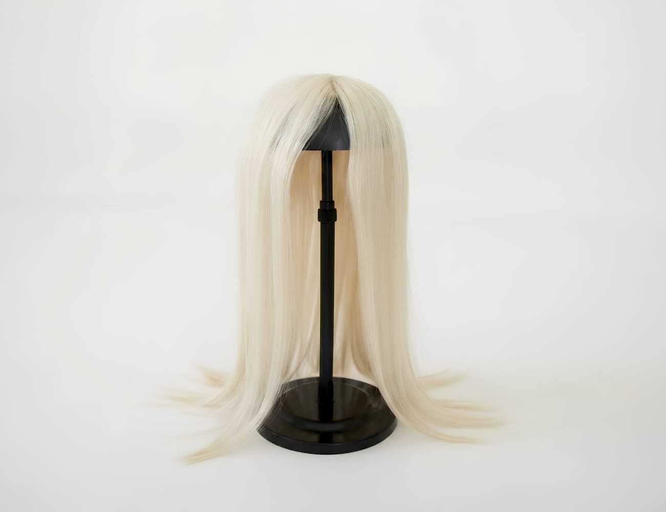 Blonde wig on a black stand against a white background.