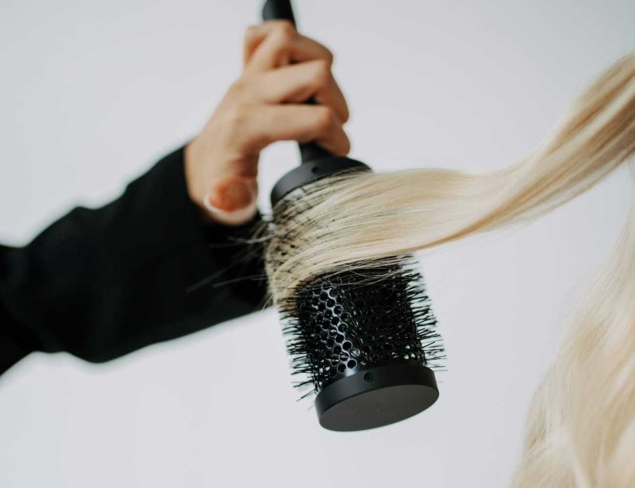 Hair stylist using round brush to curl blonde hair.