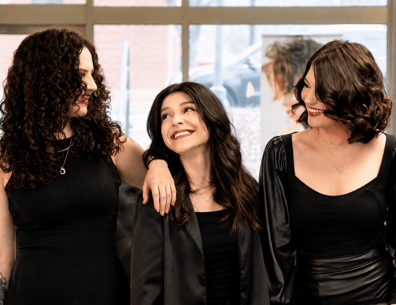 Three women in black outfits smiling and standing together indoors.
