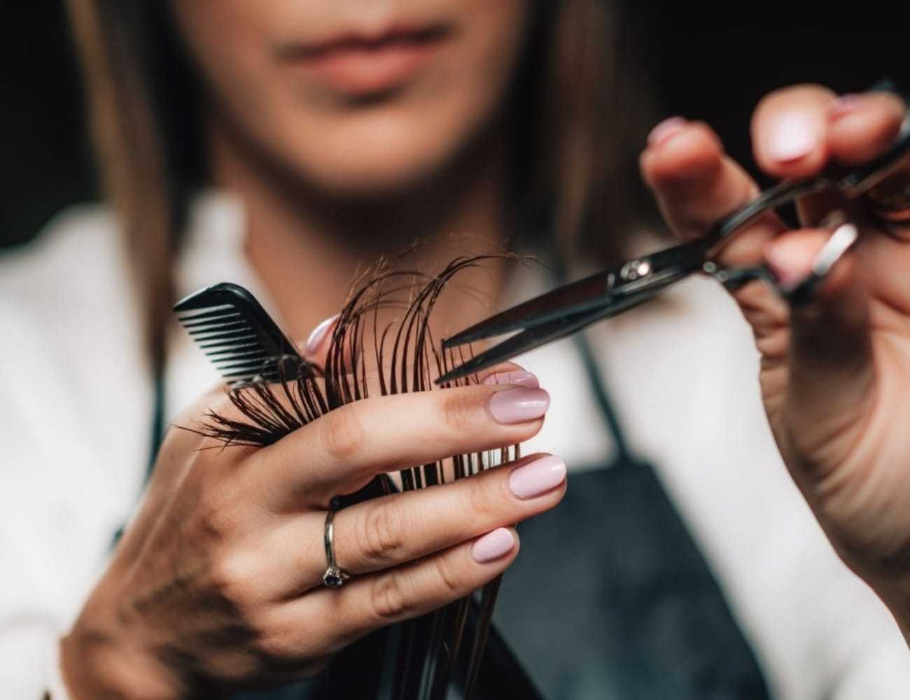 Hairdresser trimming hair with scissors and comb, close-up of hands.